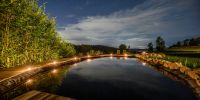 Naturteich bei Nacht unter Sternenhimmel, Kerzen am Holzsteg beleuchten das Ufer