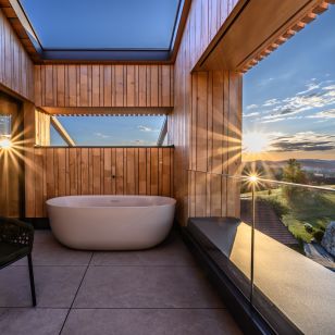 Freistehende Außenbadewanne auf der Panorama-Dachterrasse des Refugium siehm mit Holzverkleidung und Sonnenuntergang über den Hügeln